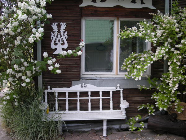 Белая скамейка, элементы отделки дома и цветущие кустарники гармонично дополняют друг друга