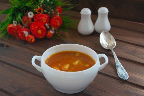 Томатный суп с картофелем, макаронами и курицей в порционной посуде на сервированном столе