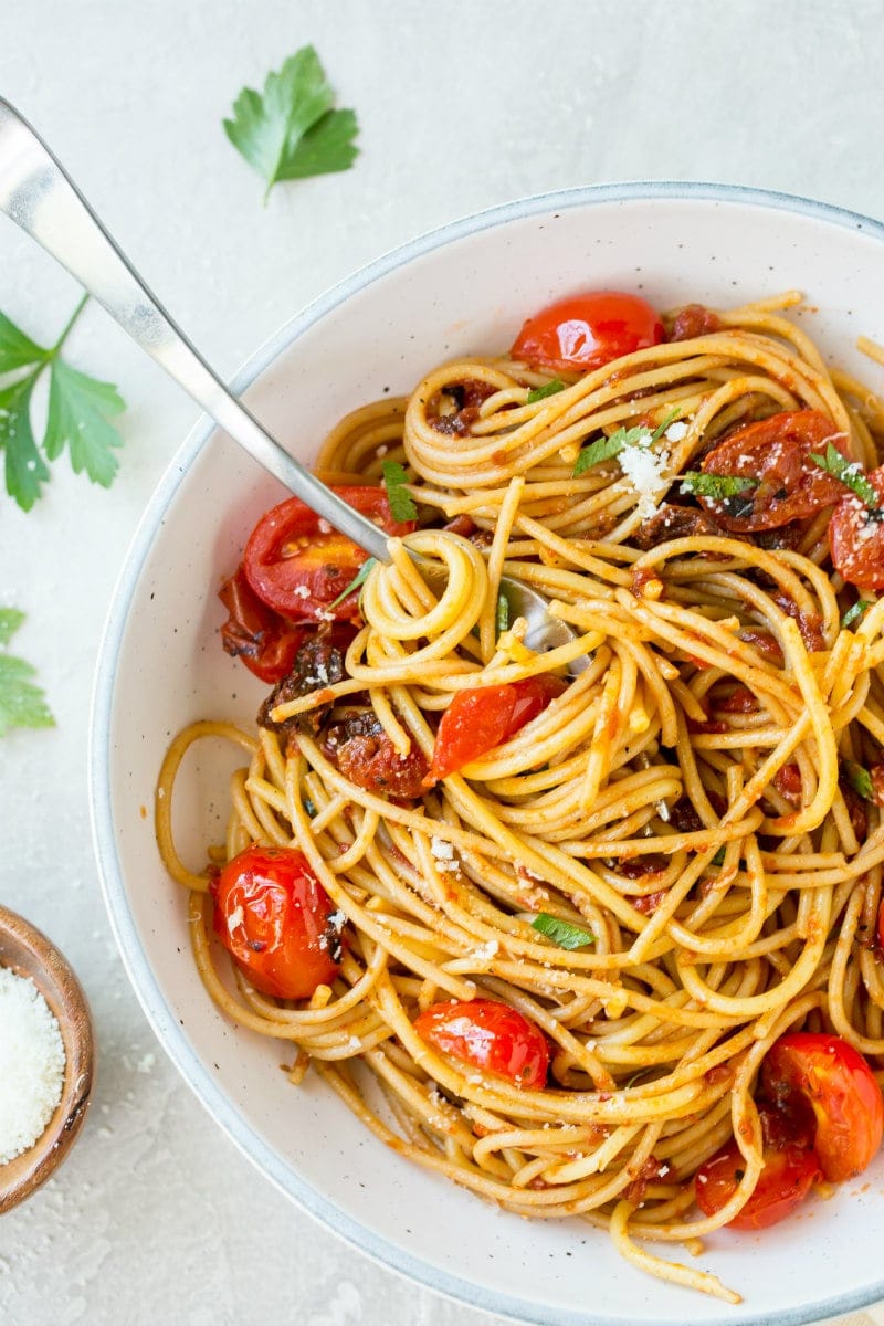 spaghetti with three tomato sauce in a white bowl with a serving spoon